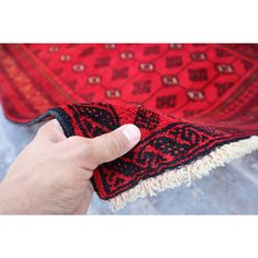 a hand holding a red and black rug