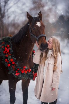 a woman kissing a horse in the snow with a wreath around her neck and nose