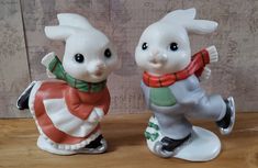 two ceramic figurines sitting on top of a wooden table next to each other