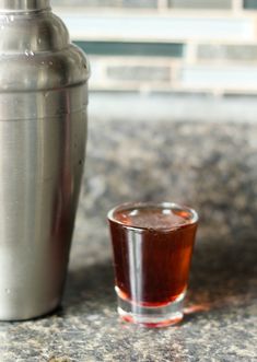 a shot glass sitting next to a metal shaker