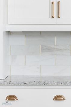 a kitchen with white cabinets and gold pulls on the cupboards, marble backsplash