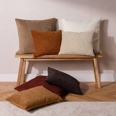 four different colored pillows sitting on top of a wooden bench next to a white wall