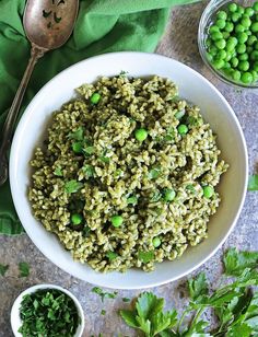 a white bowl filled with rice and peas next to some green vegetables on a table