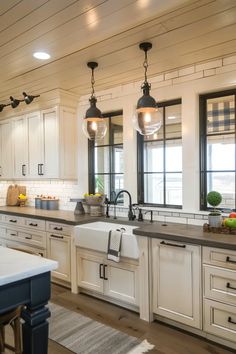 a large kitchen with white cabinets and black lights hanging from the ceiling over the sink