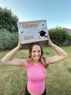 a woman in a pink top holds up a graduation cap over her head with the words senior on it