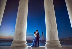 a man and woman are standing in front of pillars at night with the stars above them