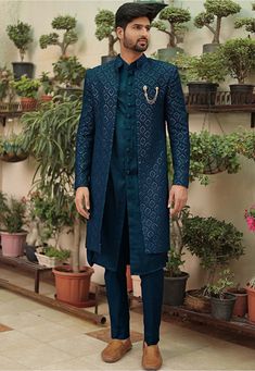 a man standing in front of potted plants wearing a blue sherve coat