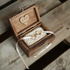 an open wooden box with two wedding rings in it on a wood bench next to a white ribbon