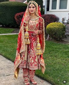 a woman in a red and gold bridal outfit stands on the sidewalk outside her home