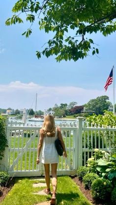 a woman walking down a path in front of a white fence with an american flag on it