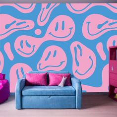 a blue and pink couch sitting in front of a wall with an abstract design on it