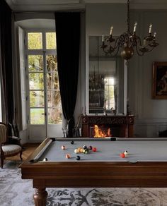 a pool table in the middle of a living room with fireplace and chandelier