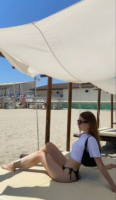 a woman is sitting on the beach under an umbrella and sunbathers are in the background