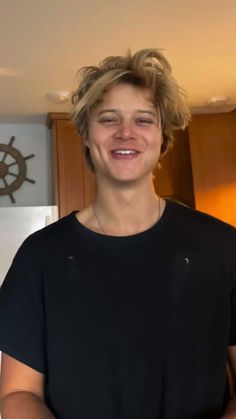 a young man with blonde hair standing in a kitchen