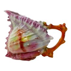 a pink and white sea shell shaped vase on a white background with an orange handle