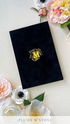 a black book with the letter m on it surrounded by white and pink flowers, including peonies