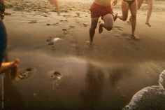 three people running on the beach with footprints in the sand and one person wearing a bathing suit