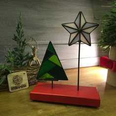 a small christmas tree sitting on top of a red stand next to a potted plant