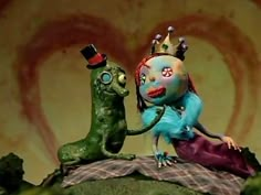 an odd looking doll is standing next to a green creature with a crown on it's head