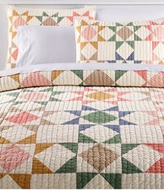 a bed with a colorful quilt on top of it next to a white headboard