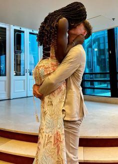 a man and woman standing next to each other in front of a staircase with their arms around each other