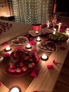 a wooden table topped with lots of plates and bowls filled with fruit next to candles