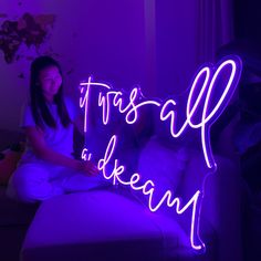 a woman sitting on a couch in front of a neon sign that reads, trust all i dream