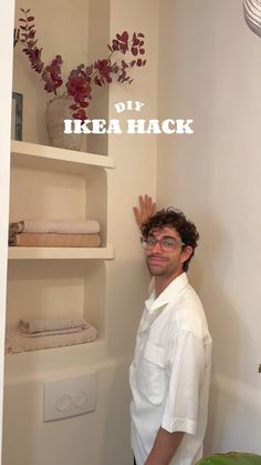 a man standing in front of a shelf with towels on it and flowers behind him