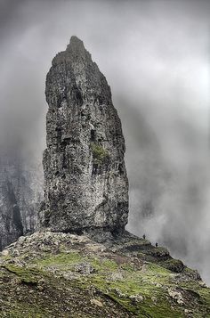 a tall rock sticking out of the side of a mountain covered in fog and clouds