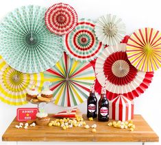 an assortment of colorful paper fans and snacks on a wooden table with popcorn, soda