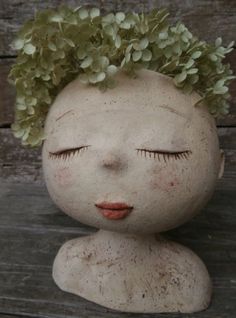 an old doll with flowers in her hair sitting on a wooden table next to a wall