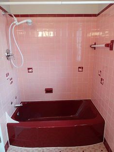 a bathroom with pink tiles and a red bathtub in the corner, next to a shower head