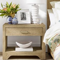 a nightstand with two vases on it next to a bed