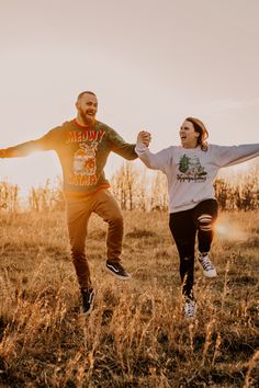 a man and woman are running through the grass holding each other's hands as the sun sets behind them