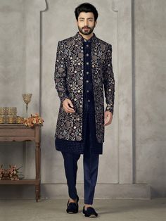 a man standing in front of a table wearing a black and blue suit with floral designs