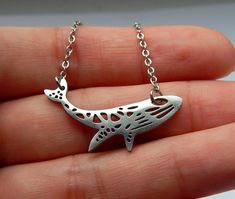 a hand holding a silver necklace with a fish on it