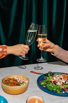 two people toasting with glasses of wine at a table full of food and drinks