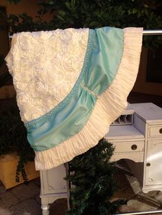 a white table topped with a blue and white blanket next to a plant on top of a wooden desk