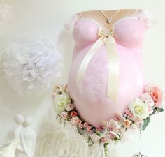 a pregnant woman's pink bra with flowers around it and a white cake in the shape of a heart