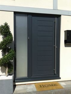 a black front door with a welcome mat on the sidewalk and potted plants outside