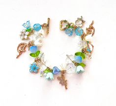 This delicate lily of the valley fairy charm bracelet is handcrafted by myself.  The gold plated chain is 7.75 inches long with a toggle clasp.  It contains flowers, a bird, butterfly,  hearts, stars and lots of crystals so it sparkles as you move.  If you need it shorter or longer just let me know, and I will adjust it to as close as possible to the size you desire.  Each charm is placed with thought  for color and balance.  It is  a really pretty bracelet, and sure to make you smile for years Whimsical Gold Charm Bracelet, Lily Of The Valley Fairy, Flower Charm Bracelet, Fairy Charms, Fairy Jewelry, Pretty Bracelets, Flower Charm, Toggle Clasp, Lily Of The Valley