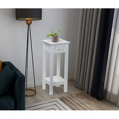 a small white table with a plant on it next to a blue couch and lamp