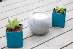 three pots with succulents and a candle on a deck