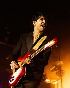 a man in a suit playing an electric guitar on stage with his mouth open and tongue out