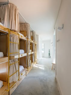 a room filled with lots of bunk beds covered in white sheets and curtains next to a wall