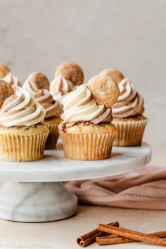 cupcakes with cinnamon butter frosting on a white cake plate next to cinnamon sticks