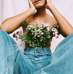 a woman sitting on the floor with flowers in her lap and holding her hands to her head