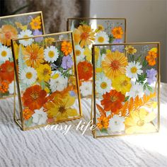 three small frames with flowers painted on them sitting on a white tablecloth covered surface