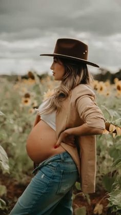 a pregnant woman wearing a cowboy hat in a sunflower field