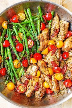 a pan filled with chicken, asparagus and tomatoes